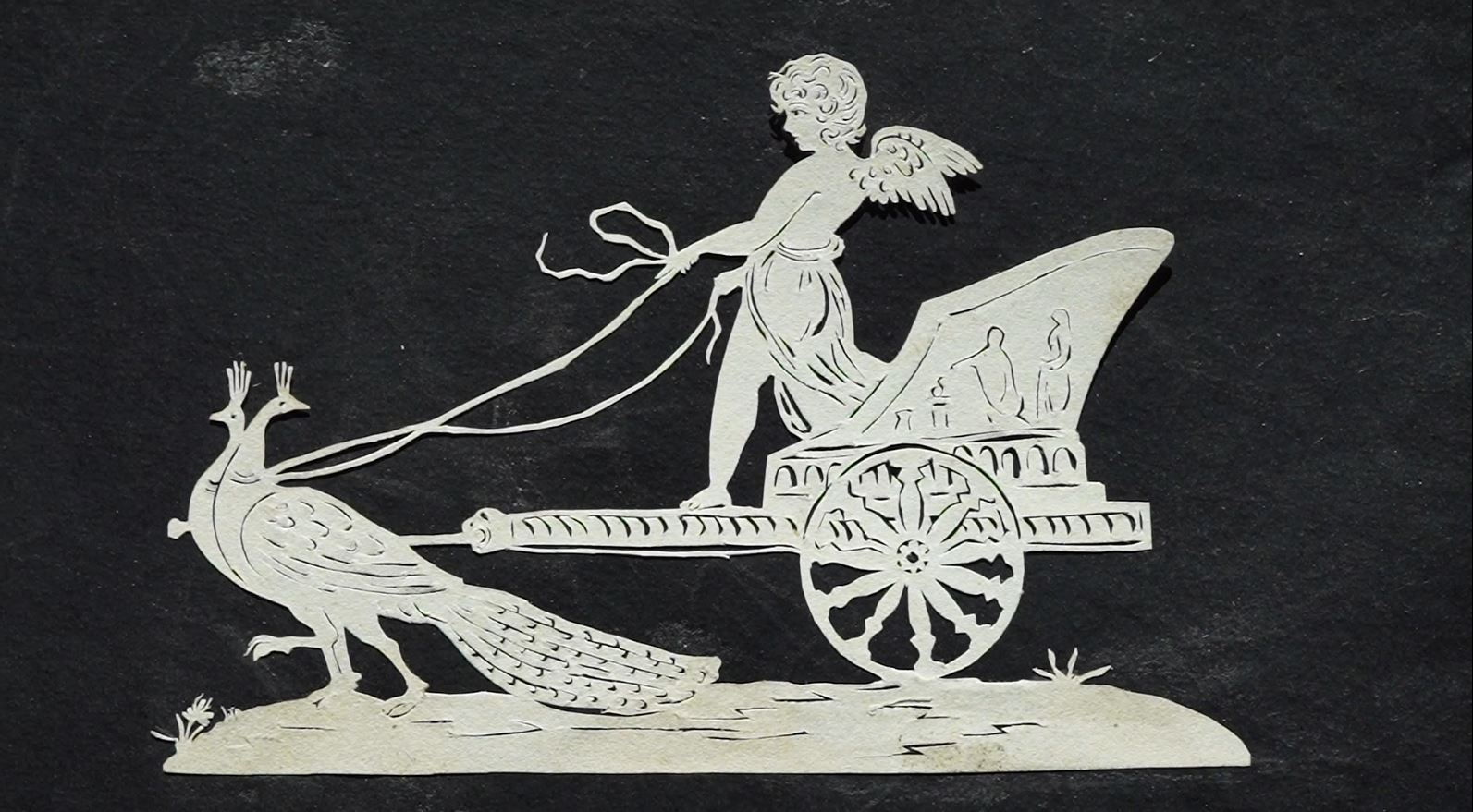 Ein Scherenschnitt, auf dem ein einachsiger Wagen mit einem Engel von zwei Pfauen gezogen wird.
